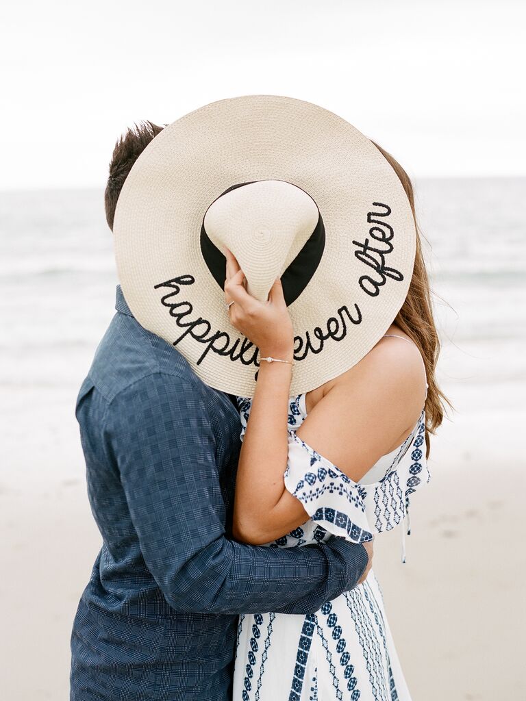 Couple kisses behind a large sun hat. 