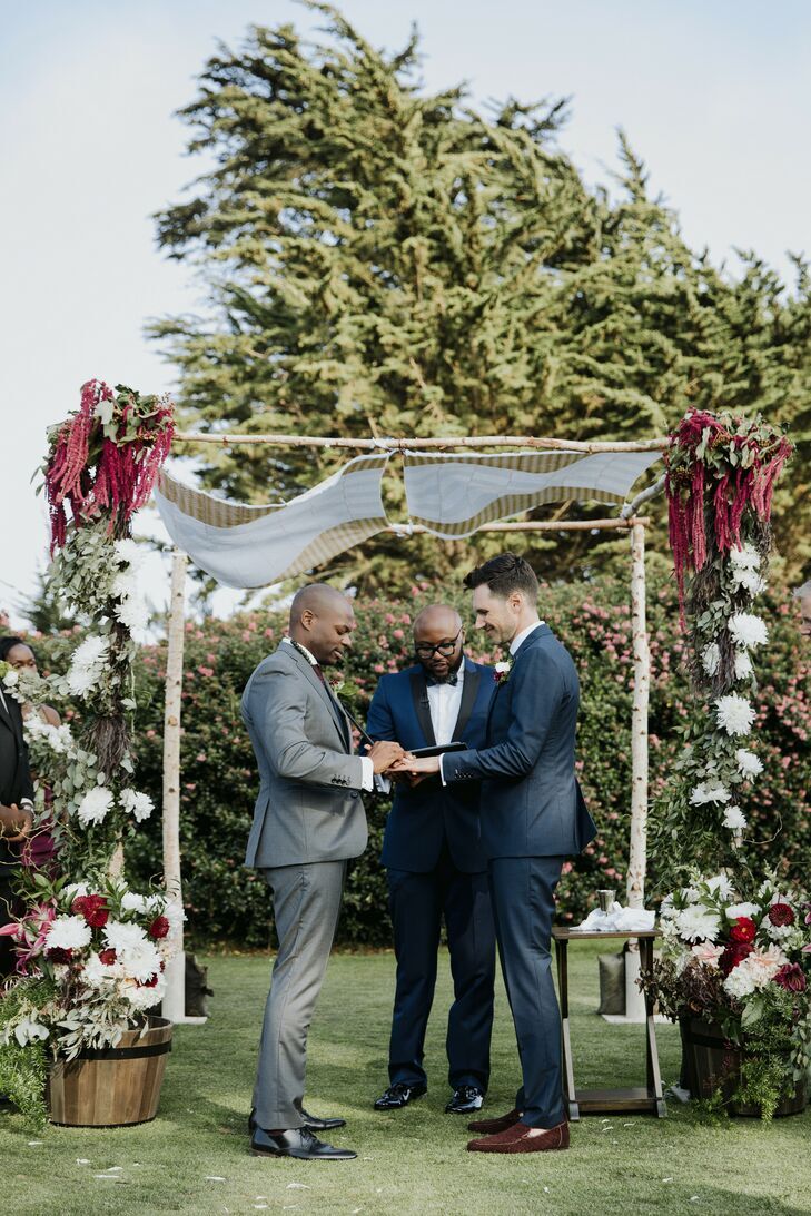 Grooms exchanging rings under birch wood chuppah. 