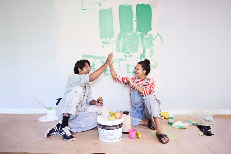 couple high fiving and painting room and smiling building confidence