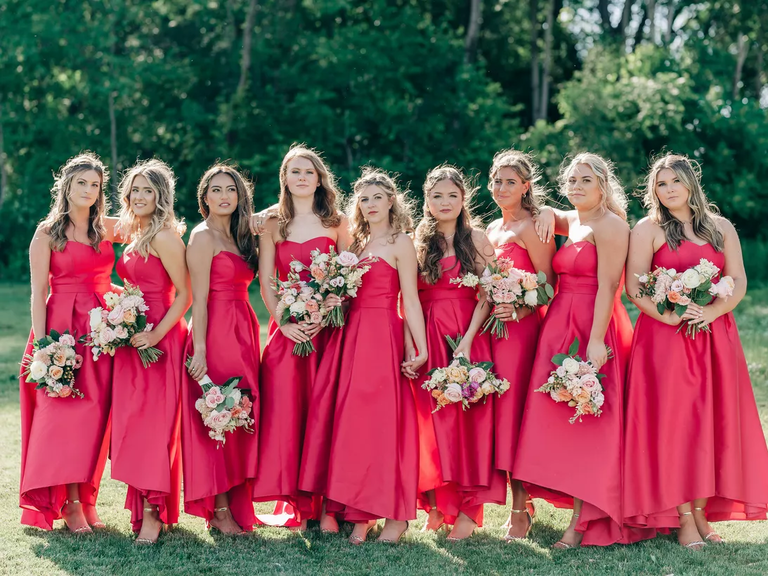 Bridesmaids stand together with their bouquets in the sun, each wearing a hot print gown.