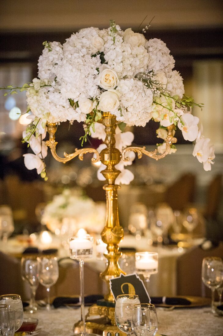 The high version of the centerpieces held white flowers spilling off of a tall gold candelabra. Candles were set all around the bottom to create a romantic light on the base of the flowers.