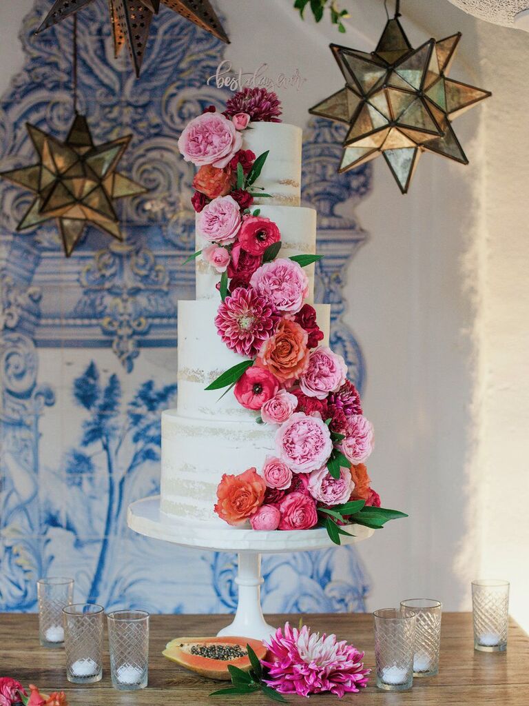 four-tier white buttercream wedding cake with bright pink and red cascading flowers