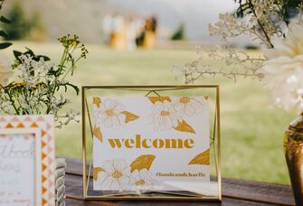 welcome sign with yellow and white floral print displayed on wedding gift table