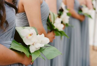 A wedding party lines up with their petite and beautiful white orchid bouquets.