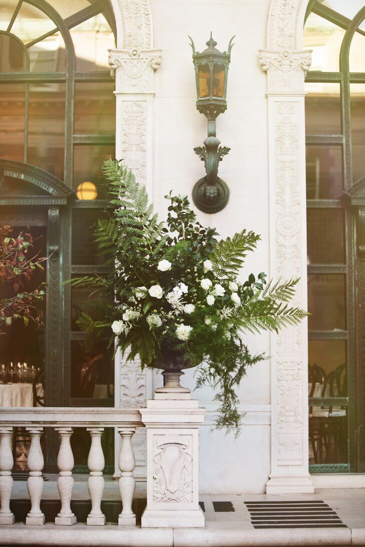 At the outdoor ceremony, lush arrangements filled with white roses and large leaves of fern were positioned on both sides of the altar where the couple were married. These arrangements also matched the smaller versions, which hung on the chairs that lined the aisle.