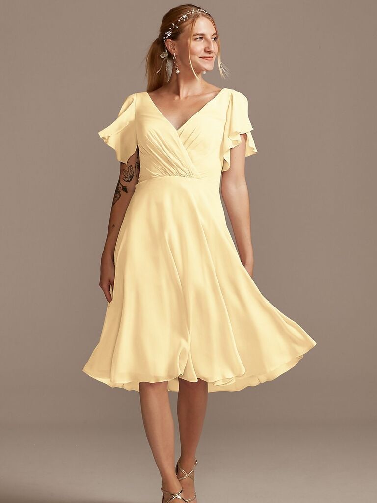 Model wears a mid-length yellow gown with a ruffled hem. 