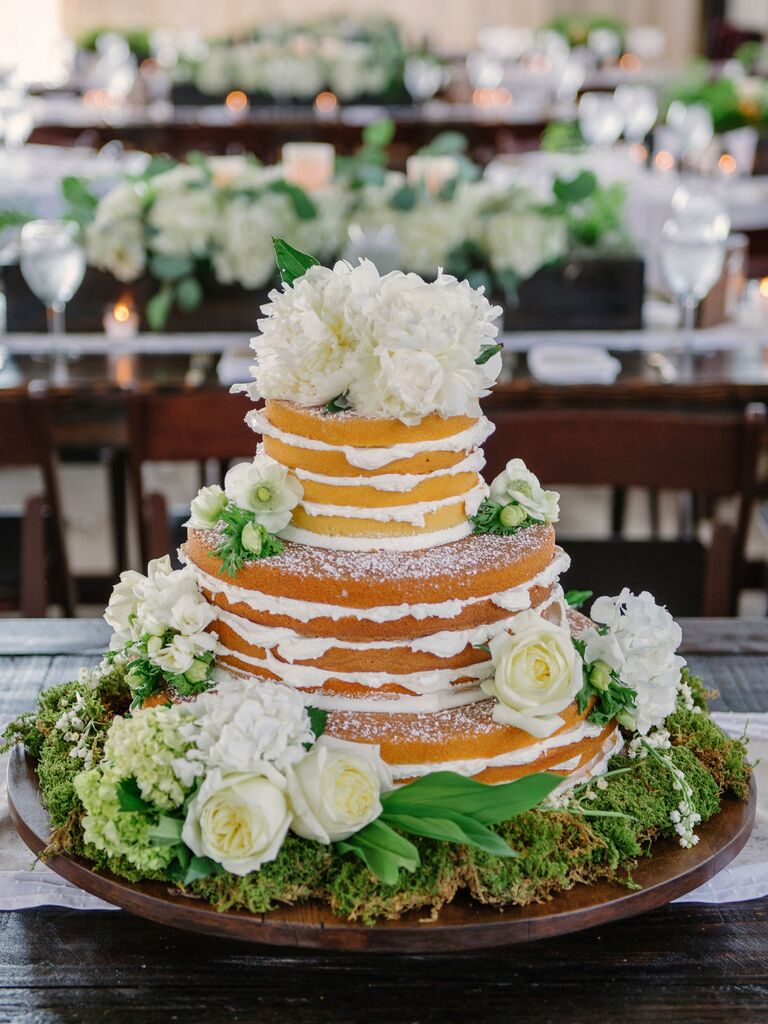 vanilla naked wedding cake decorated with white flowers, powdered sugar and moss base at the bottom tier