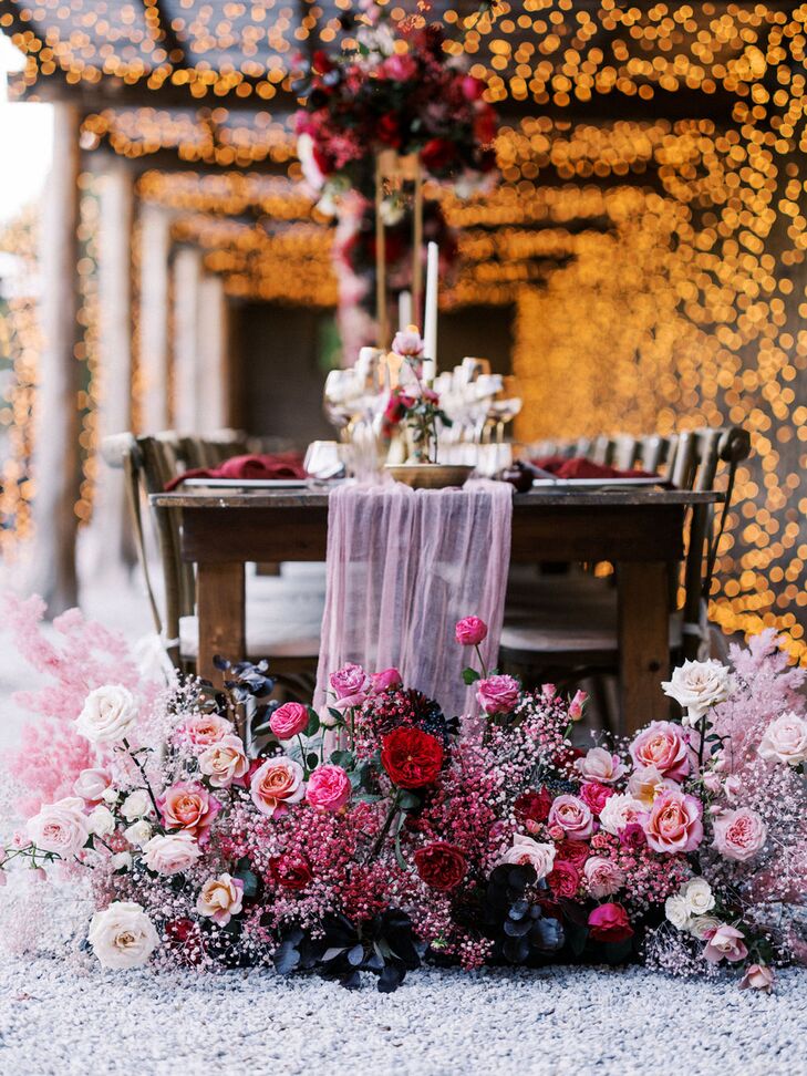 Long Wooden Table With Cascading Tulle Runner and Pink Floral Arrangements on Ground