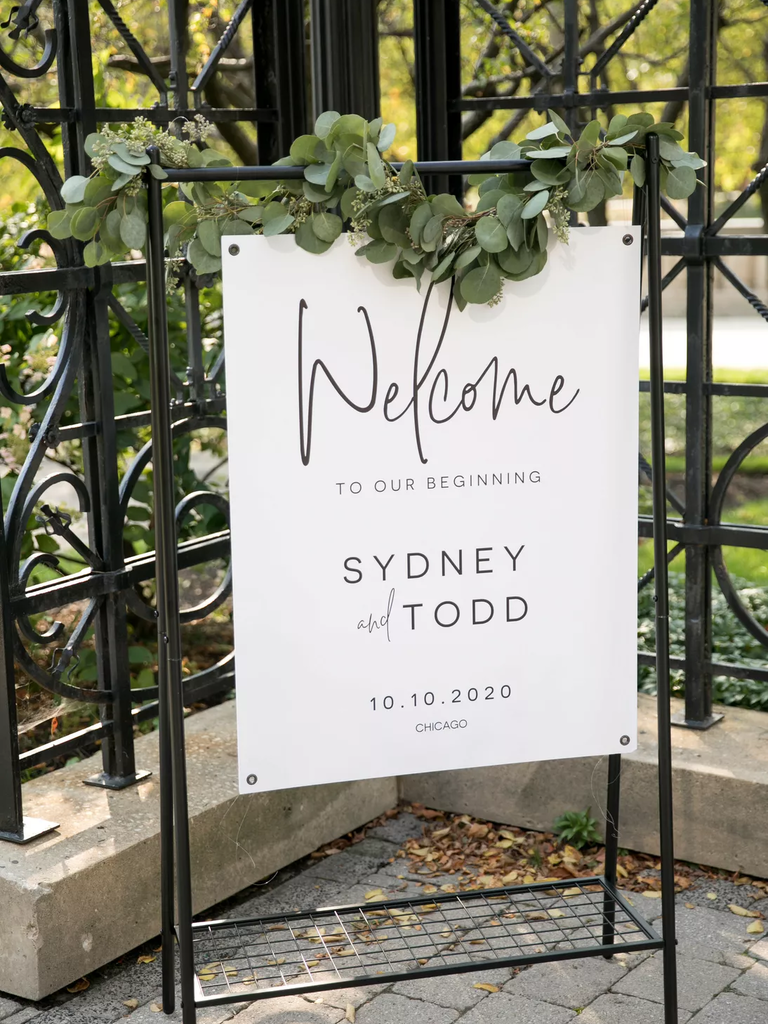 A metal easel holds a welcome sign, adorned with greenery.