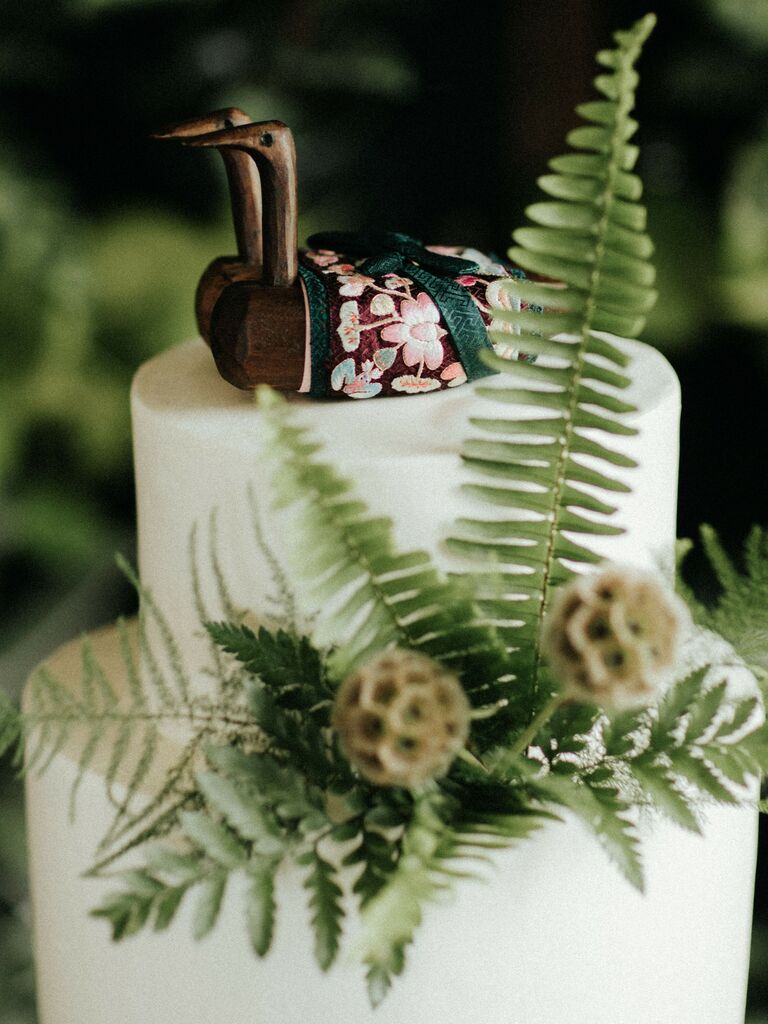 Wooden swans in cultural attire as a wedding cake topper.
