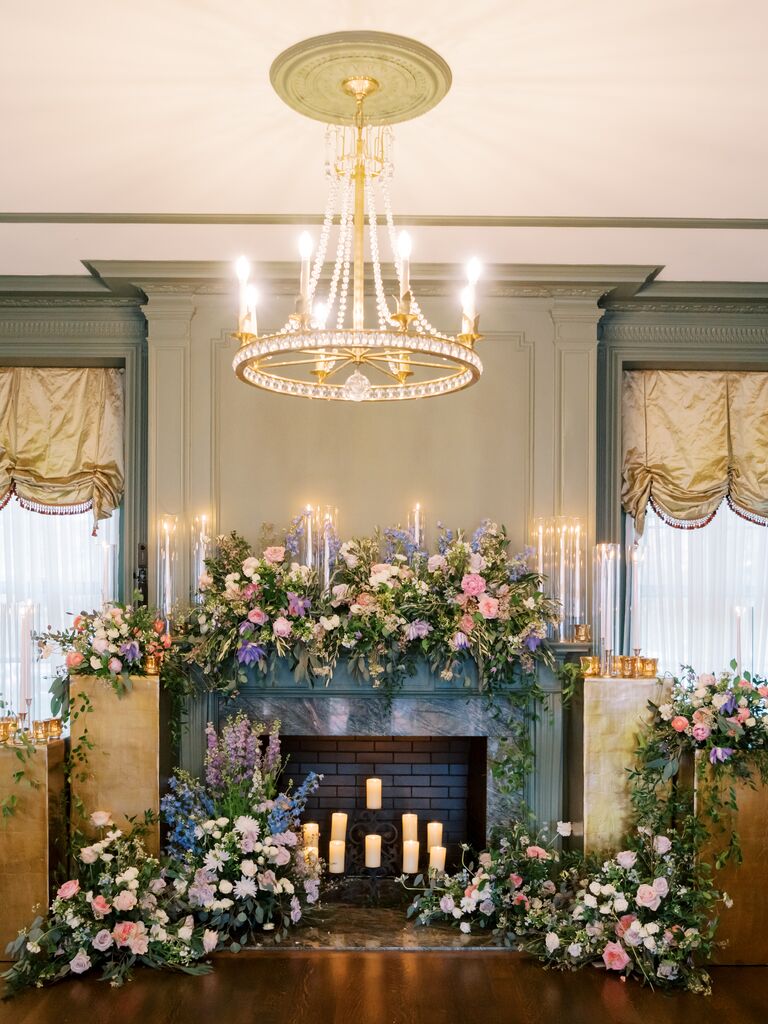 romantic wedding fireplace decor idea with pastel pink, purple and blue flowers, greenery and tall taper candles with glass covers