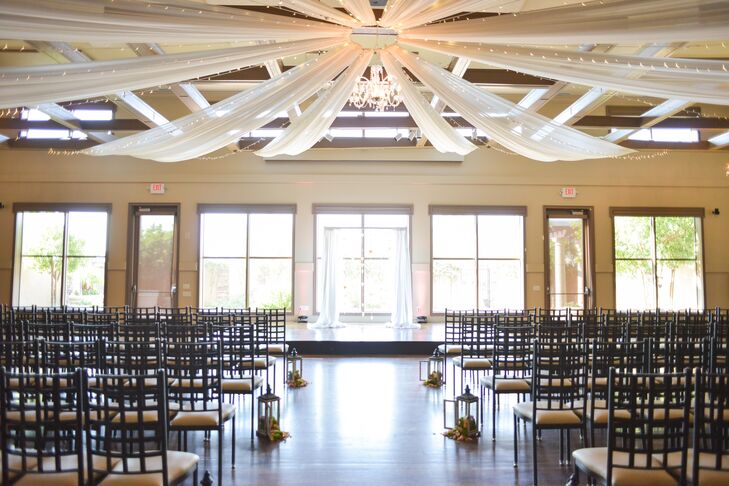 Brittney and Josh said "I do" inside the main hall, accented with dramatic drapery spread across the ceiling. A chandelier, string lights and natural light from the oversize window backdrop, as well as lanterns lining the aisle, created a soft glow in the room.