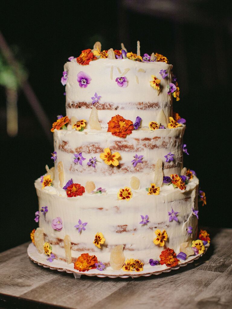 2023 wedding cake trend idea white buttercream cake decorated with purple, yellow and orange edible flowers