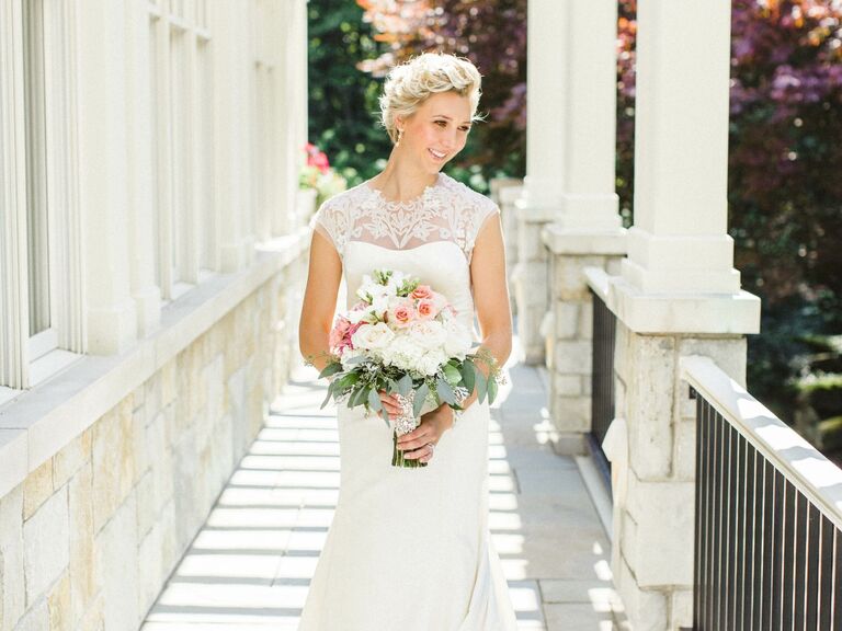 Bride wears her hair in a swept-back style while smiling and holding a bouquet of roses. 