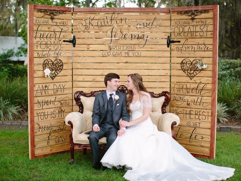 Couple poses in front of custom wooden photo booth backdrop. 