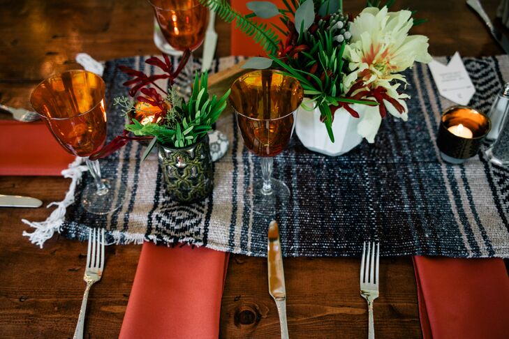 Each table rocked the couple’s free-spirited themes with bold colors. They matched the handcrafted wooden tables with printed yoga blanket runners. Poppy-colored napkins marked each place setting alongside orange-accented stemware. Of course, they also included a few natural elements such as ferns, eucalyptus, silver brunia and white peony centerpieces. Low tealight candles highlighted each piece of decor.
