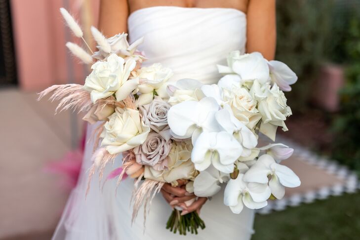 A classic white, asymmetrical bridal bouquet featuring roses, orchids and bunny tail grass with cream, blush and lavender accents at a mid-century modern wedding.
