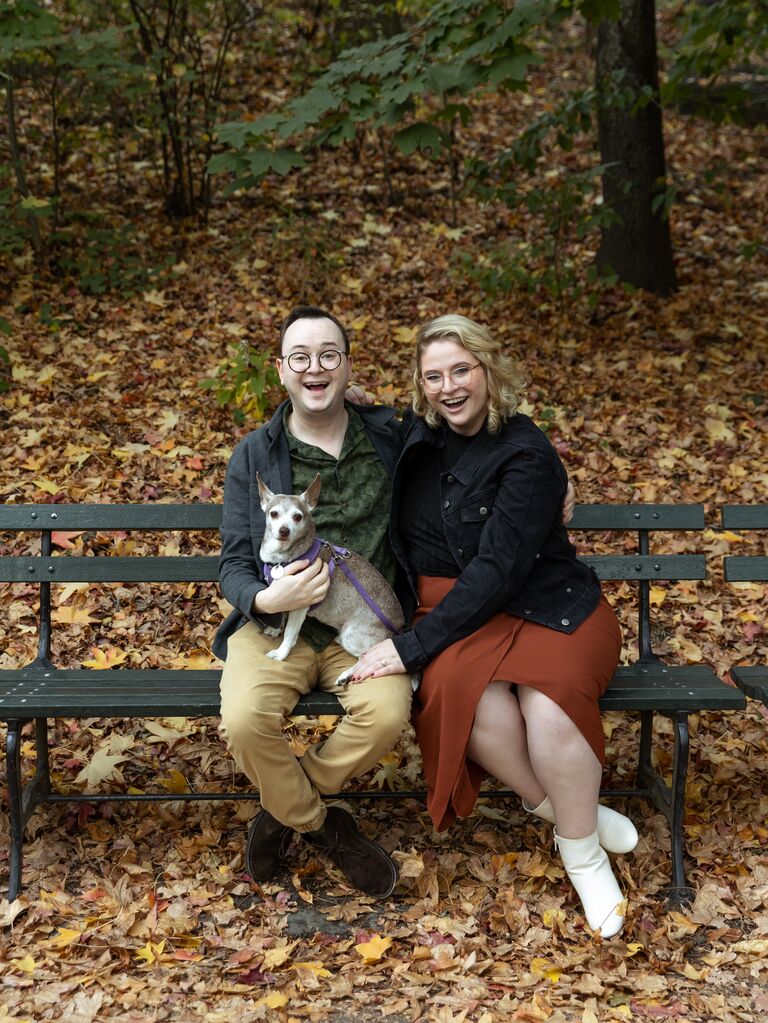 Couple smiling in the park with their small dog.