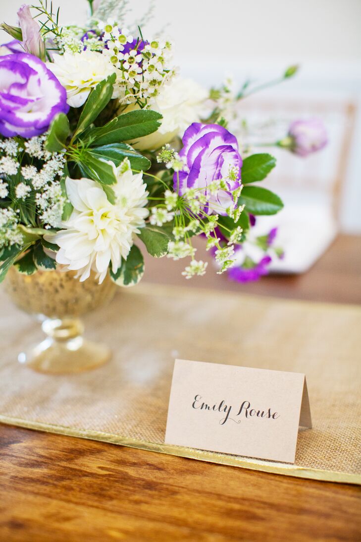Table centerpieces included purple anemones, white roses, white dahlias, purple mini calla lilies, and berries held in gold bowls. Hand-calligraphed place cards noted each guest's seat.