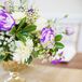 Table centerpieces included purple anemones, white roses, white dahlias, purple mini calla lilies, and berries held in gold bowls. Hand-calligraphed place cards noted each guest's seat.