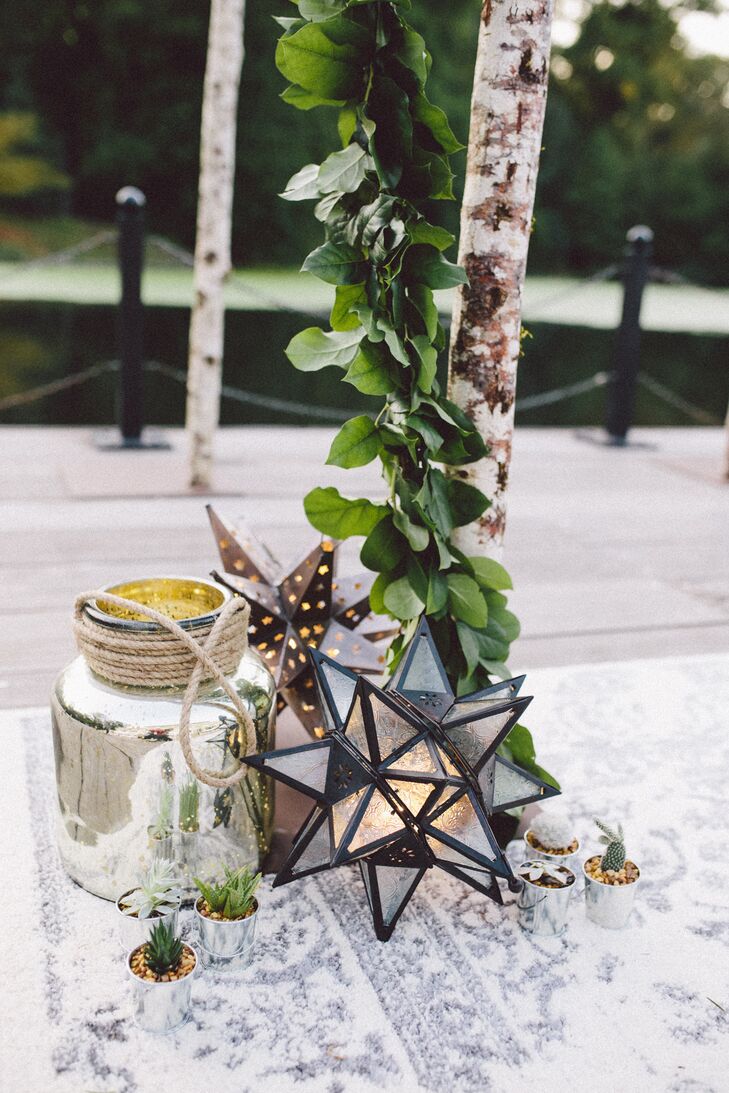 Cacti, Mexican star lanterns and mercury glass vases rested at the base of the birch wedding arch, which stood atop a rug and was wrapped in a live salal garland.