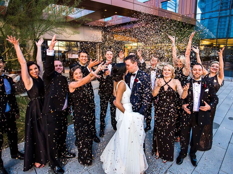 Bride and groom kissing under confetti toss thrown by wedding party