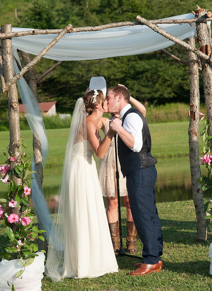 Mary and Sam shared their first kiss as husband and wife under a rustic wooden arch made out of tree branches and decorated with white drapery and pink flowers.