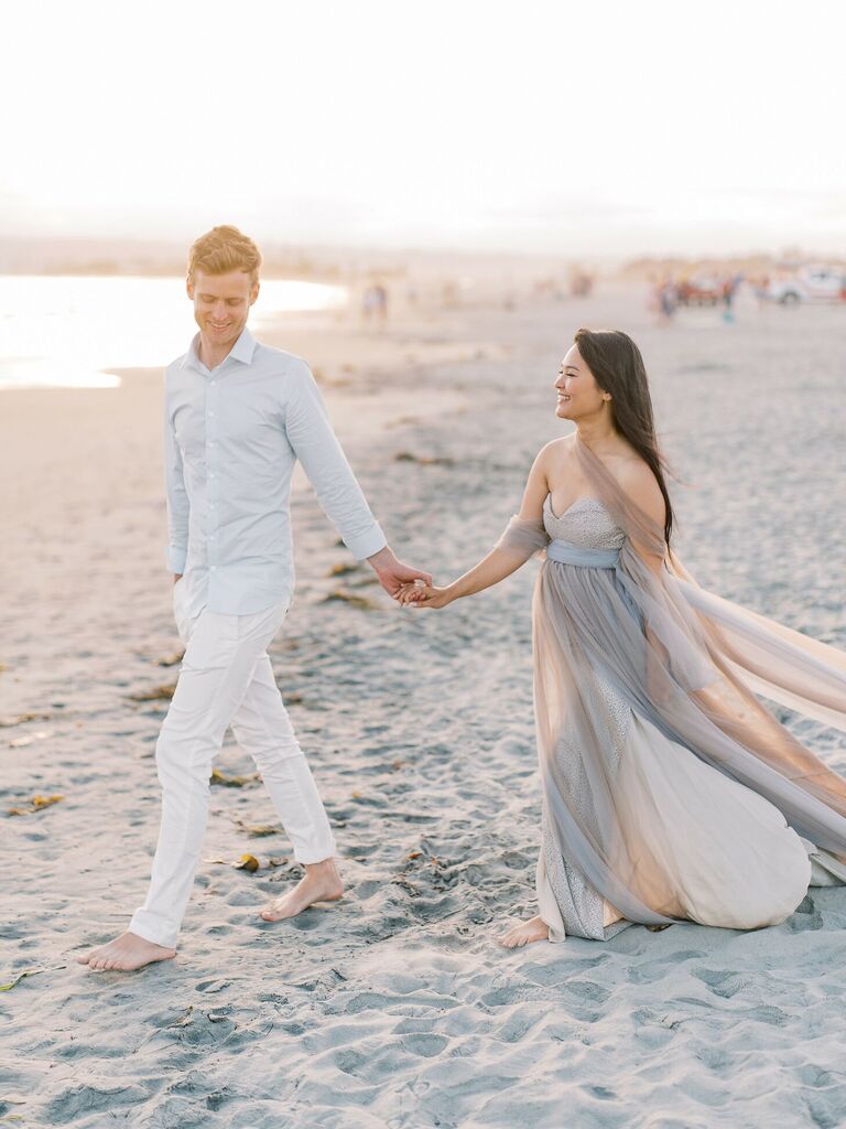 Couple walks hand-in-hand on beach during sunset