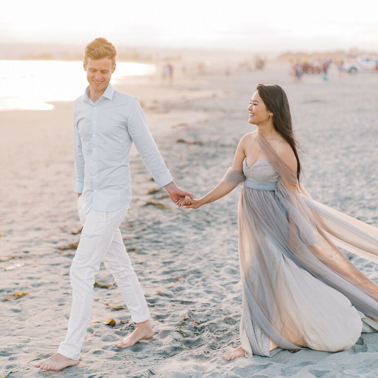 Couple walks hand-in-hand on beach during sunset