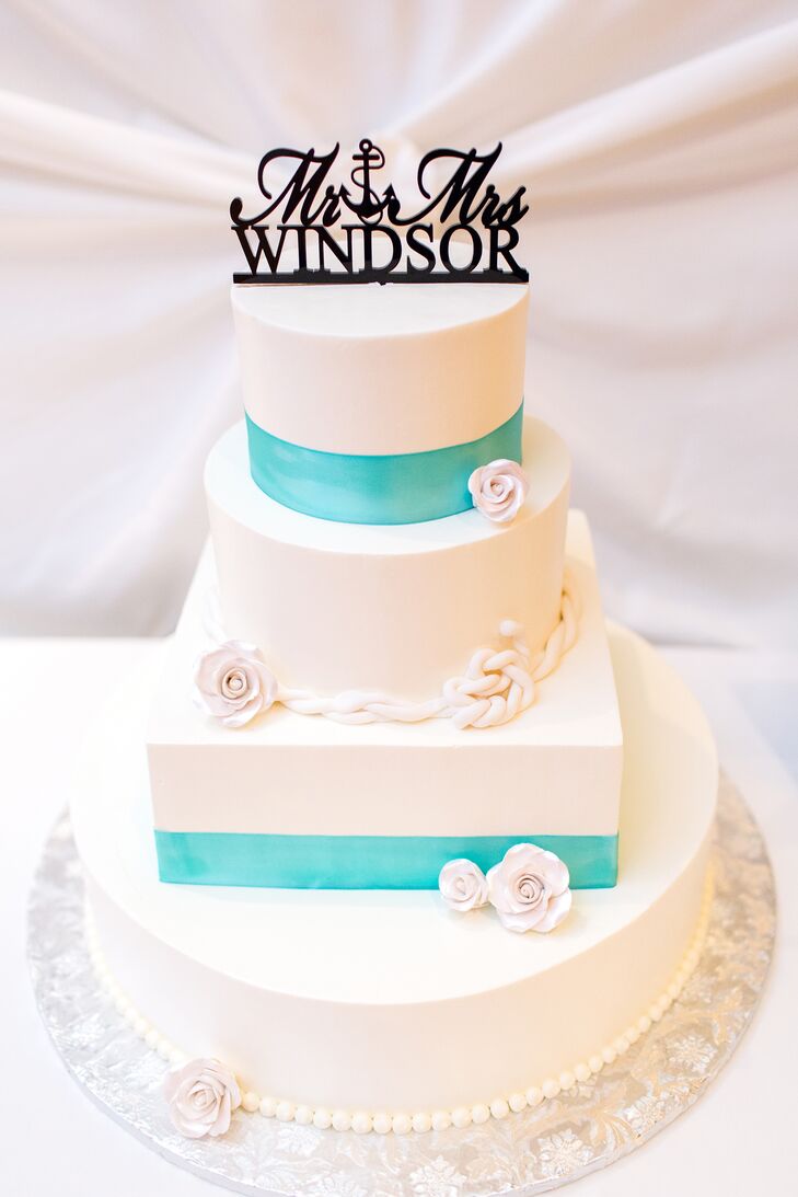 The white wedding cake had three round tiers and a square middle tier. The cake was decorated with white cake flowers and a fondant rope accent. It also featured turquoise ribbon accents and a nautical-themed cake topper.