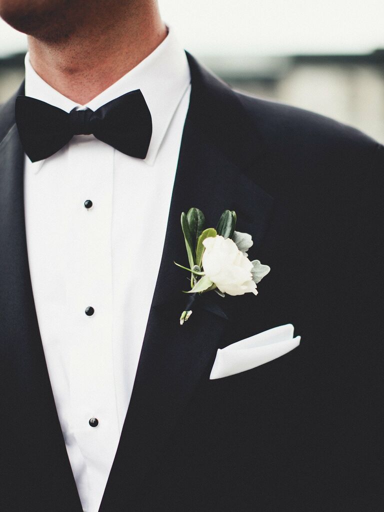 groom wearing classic black tuxedo and bow tie with single white flower boutonniere and matching pocket square