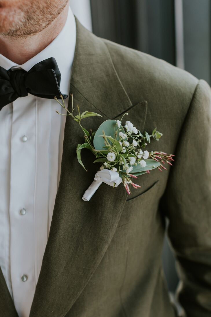 Groom in Green Suit Jacket Shows Boutonniere With White Flowers, Greenery