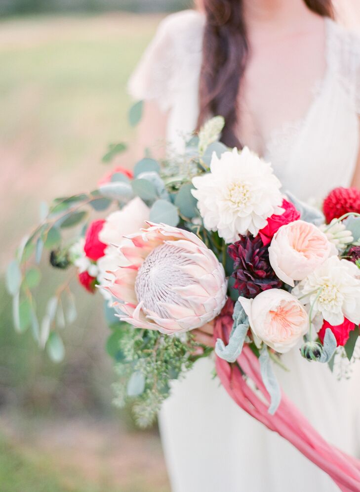 Michelle carried a bouquet of white and red dahlias, seeded eucalyptus, blush garden roses, dusty miller and scabiosa pods down the aisle . A blush king protea stood out within the arrangement.  “I knew I wanted a very large bouquet since my dress was simple,” says Michelle.
