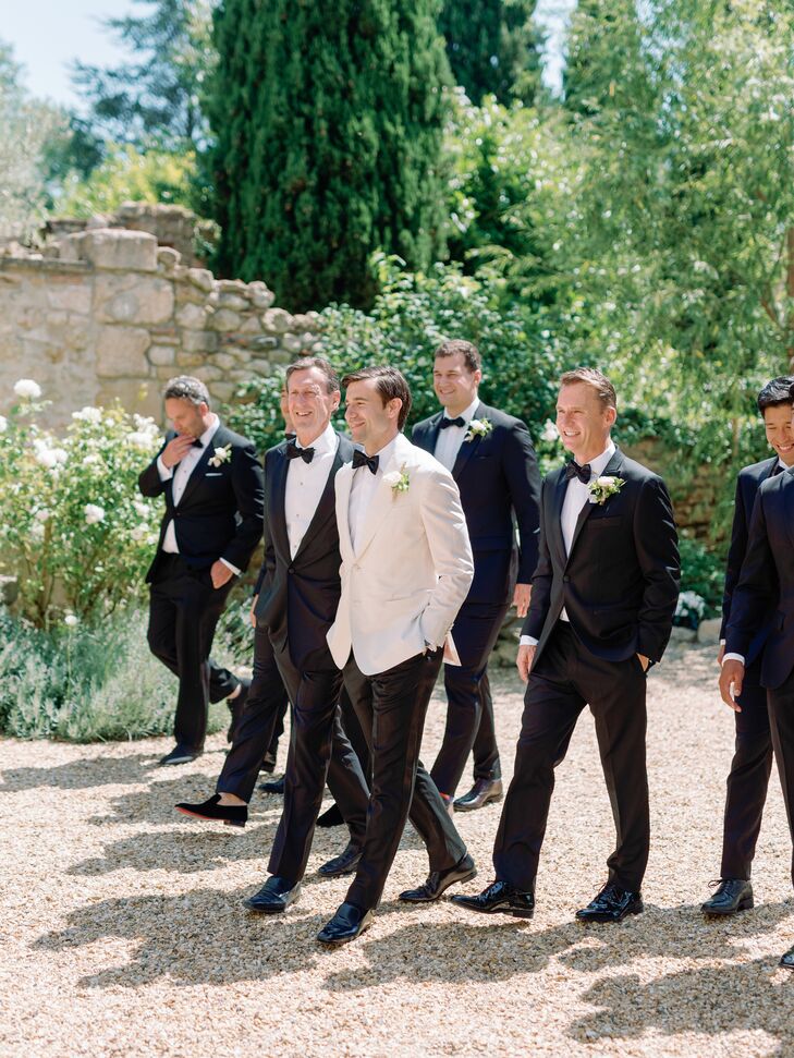 Groom in White Tuxedo Jacket Walking With Groomsmen in Classic Black Tuxedos and White Boutonnieres