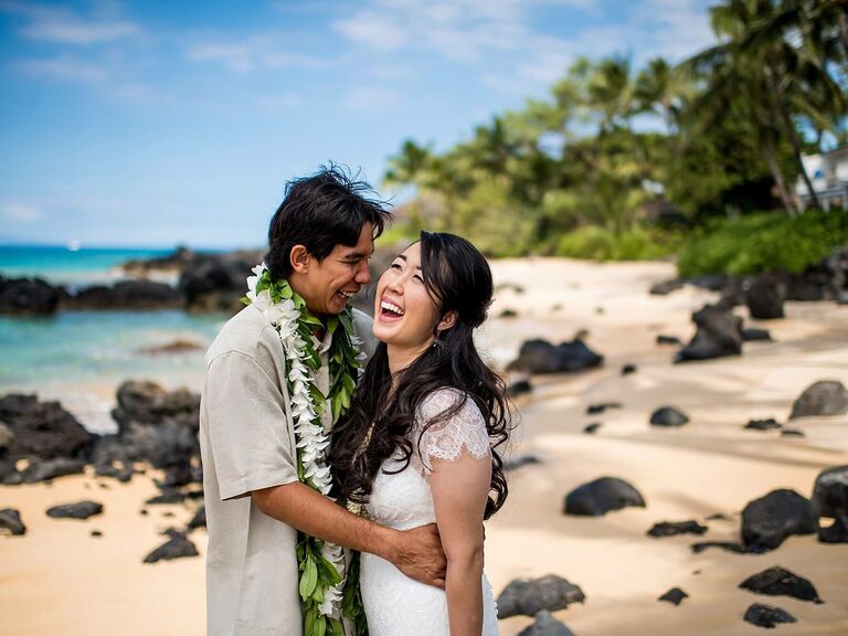 Couple laughs while embracing on a beach. 