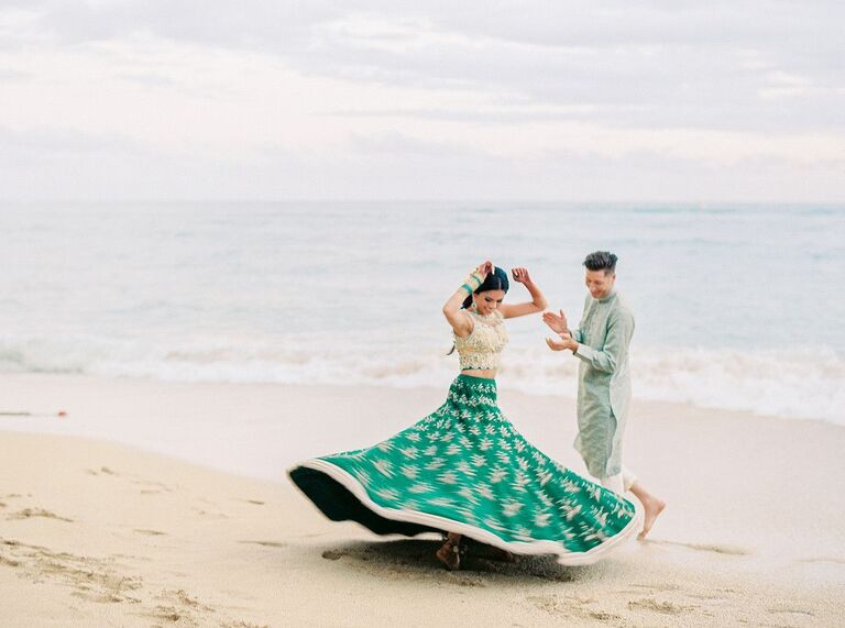 Bride twirling in wedding dress on the beach while groom claps