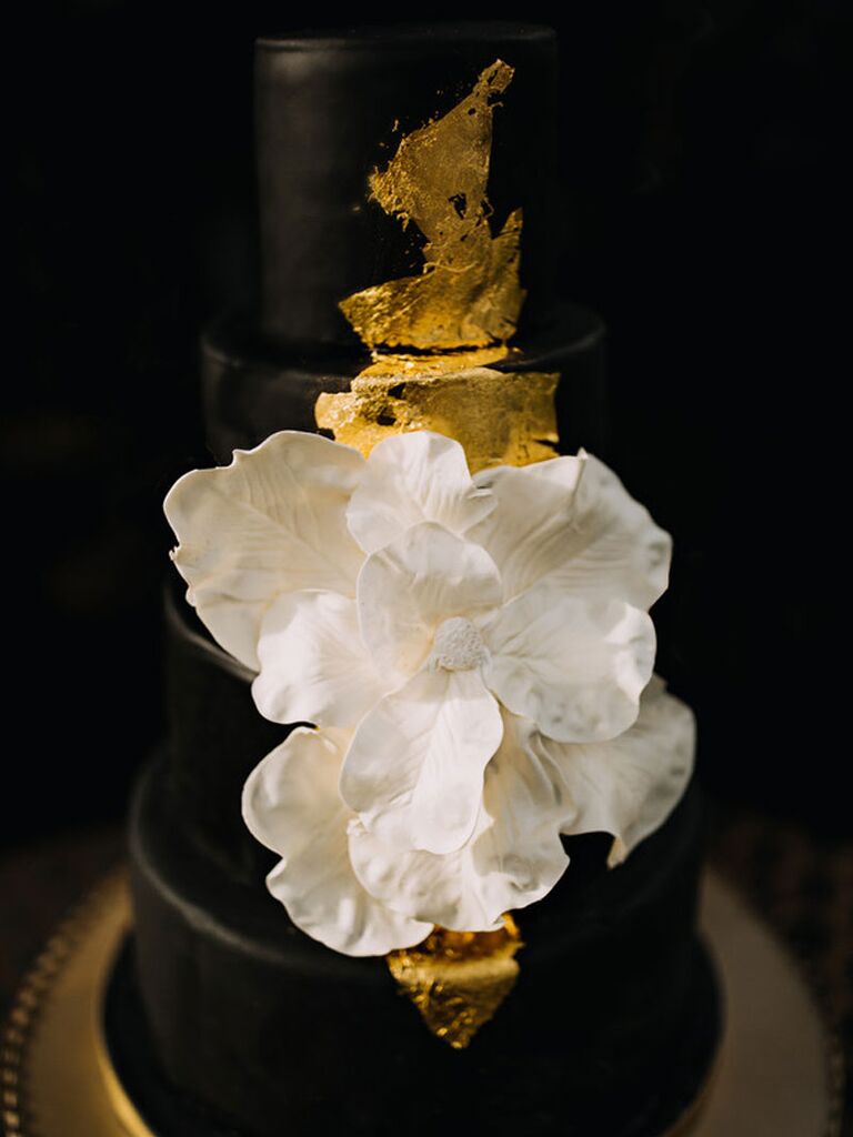 Black four-tier wedding cake with gold foil and large while flower