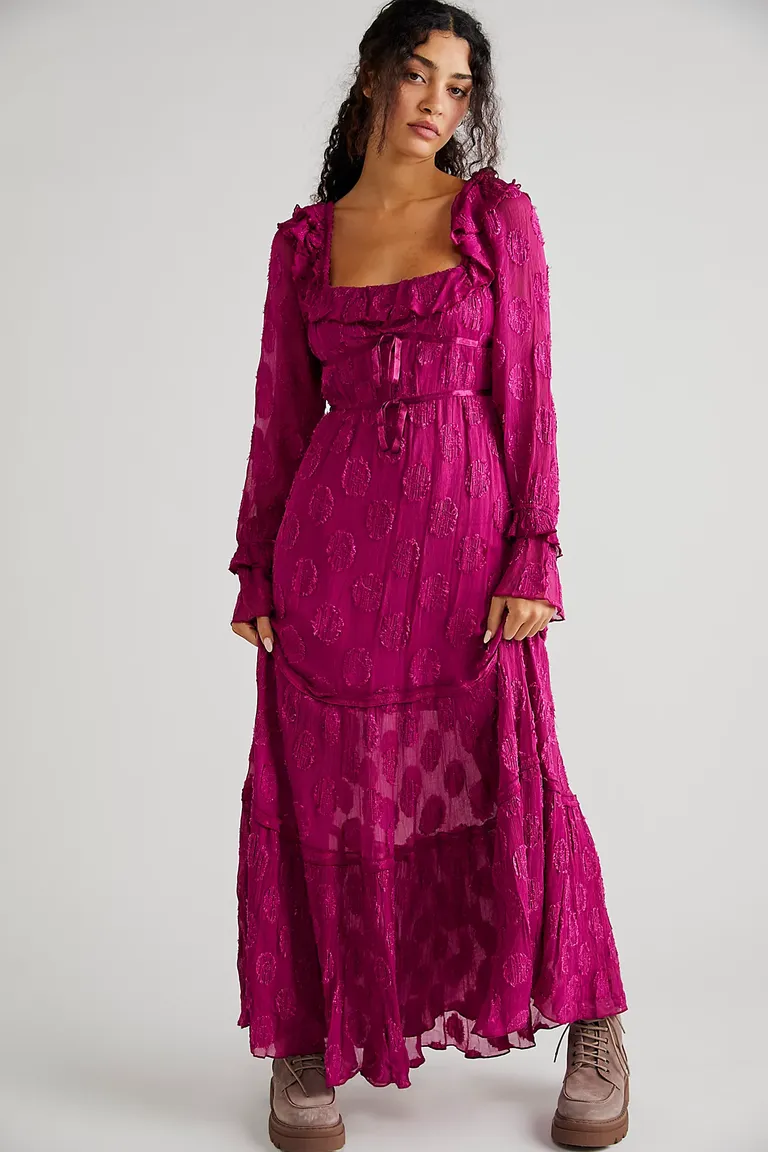 Model wears a fuschia-colored dress with long sleeves and a ruffled neckline. 