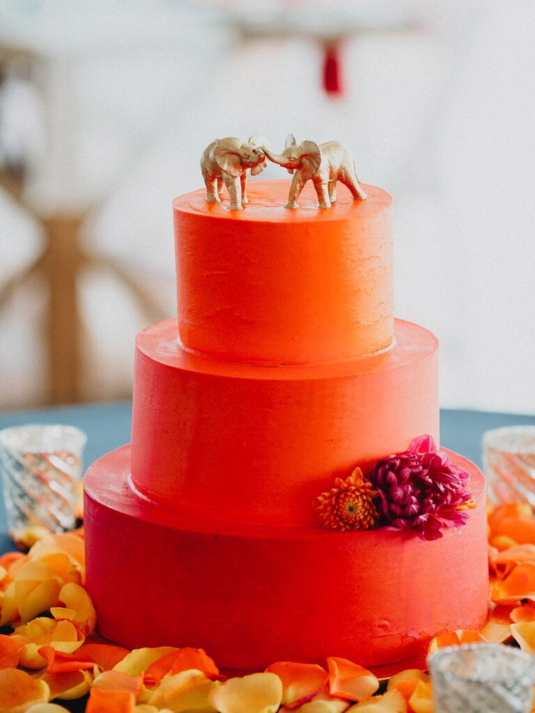 Two golden elephants on top of an orange three tier cake. 