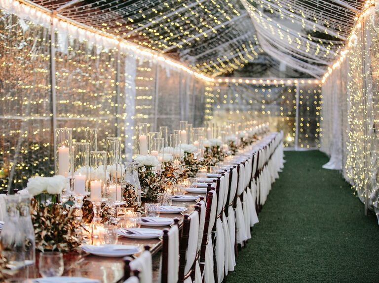 long wedding reception table surrounded by clear tent covered with string lights