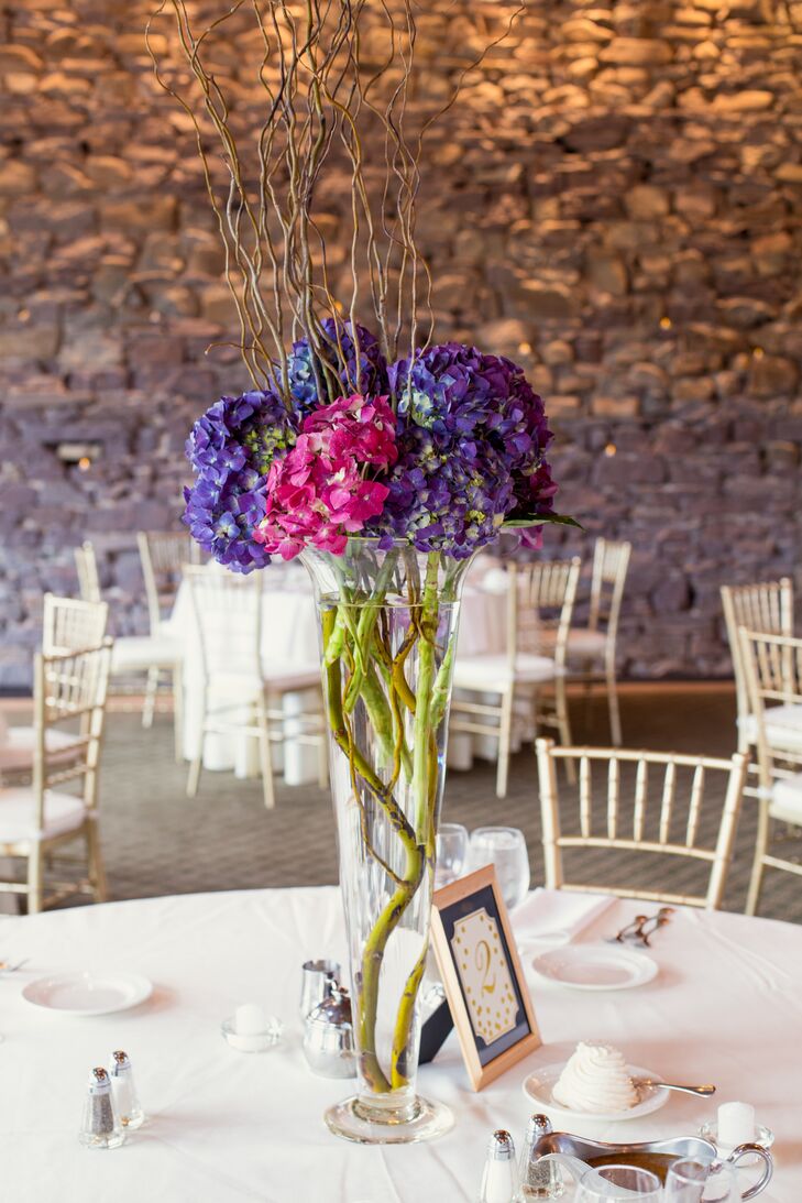 The team at Chantilly Floral Boutique made eye-catching arrangements for the couple’s reception and added a whimsical flair to the day. Purple hydrangeas were mixed with pink hydrangeas and two types of branches in tall trumpet of low cylinder vases. Each added an unexpected accent to the La Massaria at Bella Vista’s exposed-brick walls.