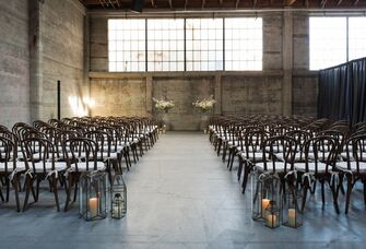 indoor wedding ceremony at minimalist industrial warehouse venue with large factory windows and concrete walls