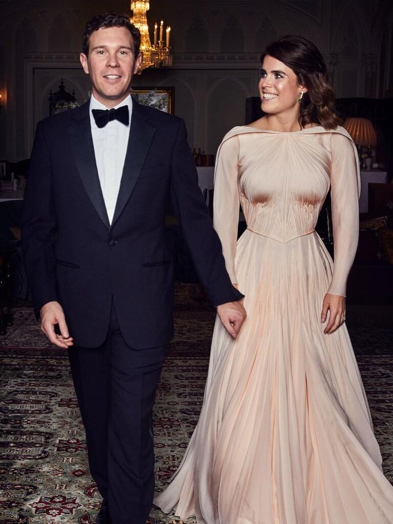 Princess Eugenie wears a cream colored long-sleeved ball gown while holding hands with her husband. 