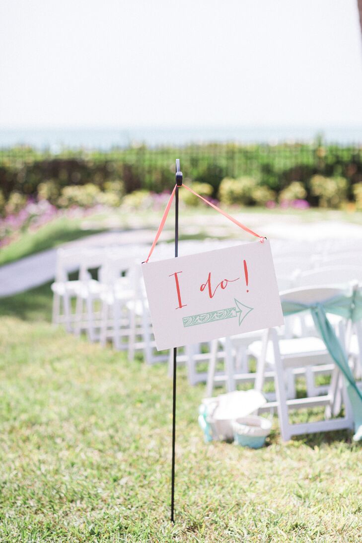 Guests were pointed to the outdoor ceremony with a sweet sign. The accent brought out their coral and mint wedding colors with a calligraphy “I do” and intricate mint arrow that resembled the waves on their stationery.