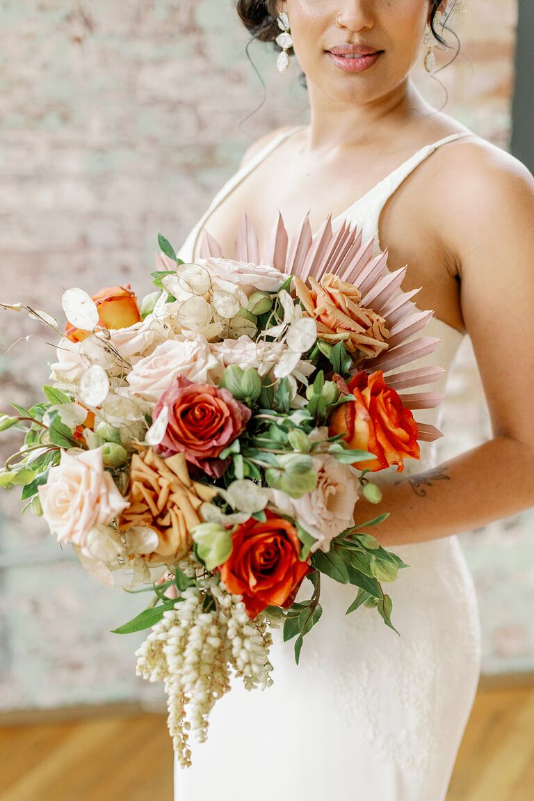 bohemian wedding bouquet showcasing 2022 wedding colors with orange roses greenery and pale pink sun palms