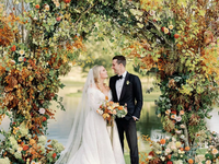 A bride and groom share a moment together beneath an autumnal archway.