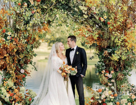A bride and groom share a moment together beneath an autumnal archway.
