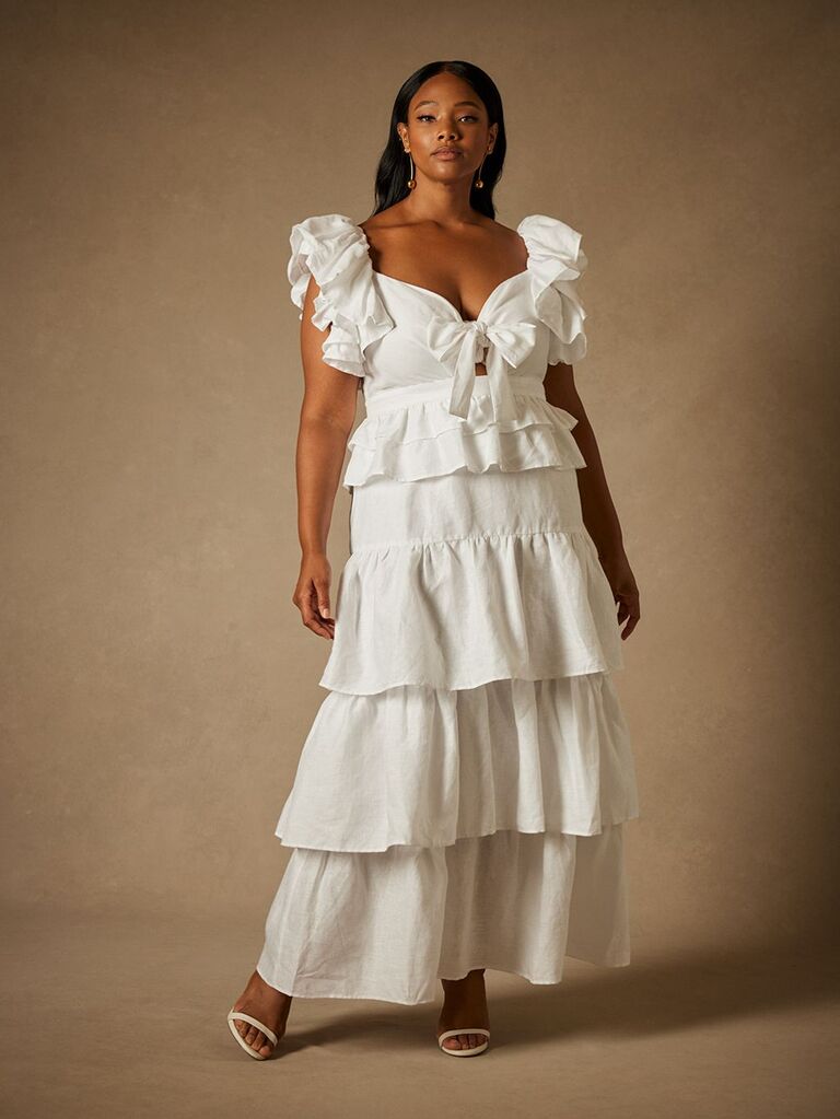 Model wears a white gown with ruffled tiers. 