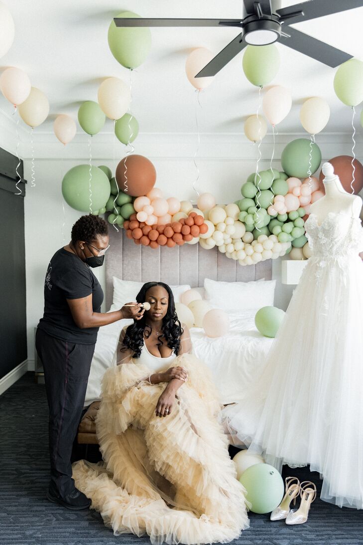 Bride in Tulle-Trim Champagne-Colored Robe With Balloons Getting Makeup Done