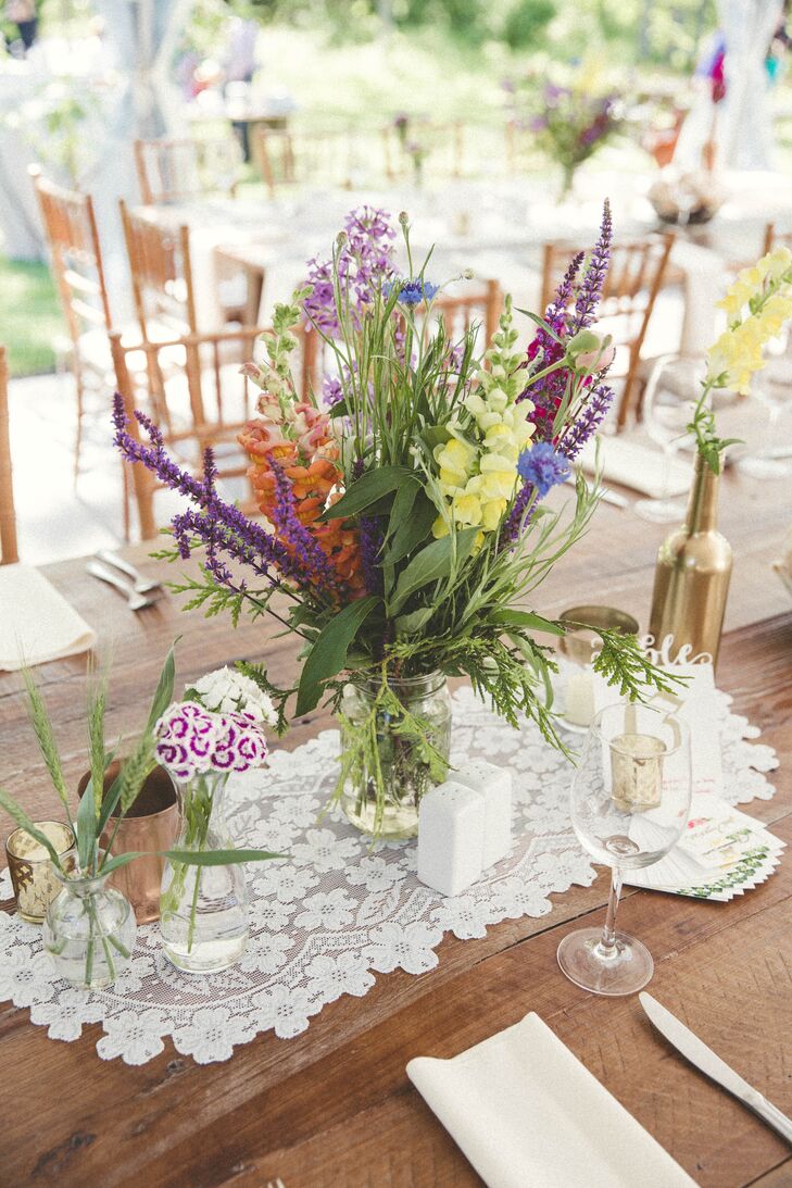 All the decor for their chic tented reception was DIY. Lauren and her mother handpicked each glass vase, bottle, jar and cup for the centerpieces. They even spray-painted a few gold or copper to add some dimension to the table. Lavender, orange delphiniums, wildflowers, greenery and yellow lilies from the valley filled each one for a bright, natural touch.